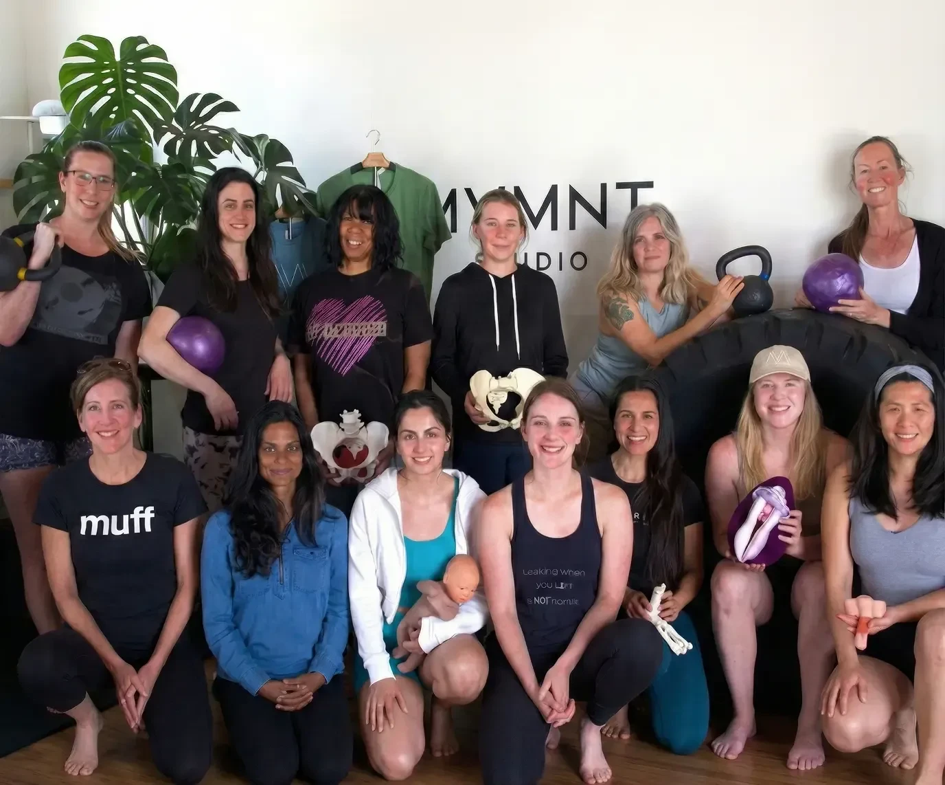 A group of smiling women at a Buff Muff pelvic floor workshop, holding pelvis models